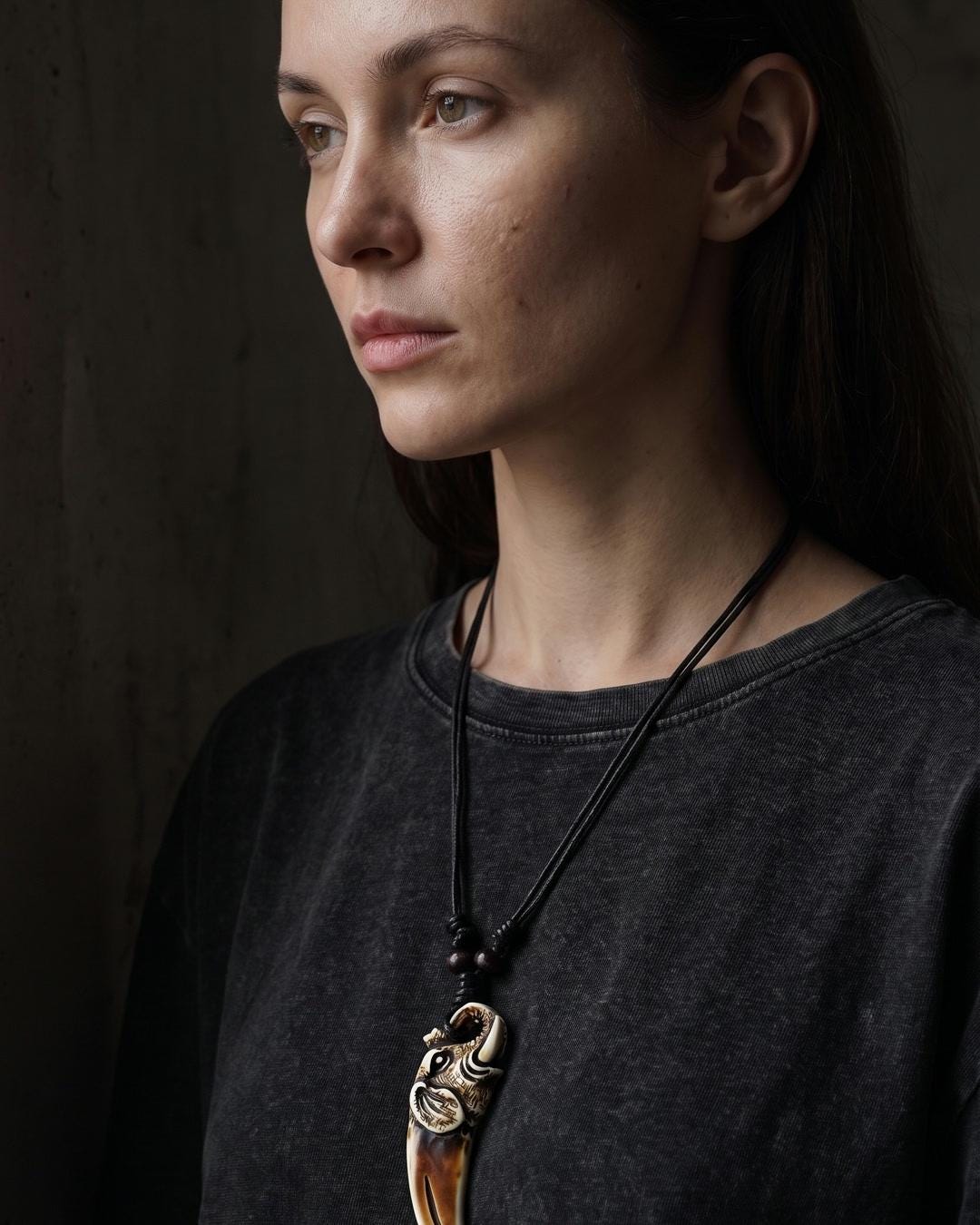 Carved dragon tooth pendant necklace lying flat on a dark surface with wood beads and black cord visible