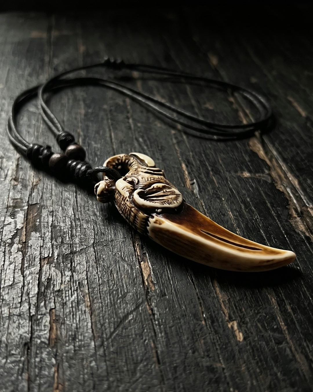Close-up of a carved dragon tooth pendant necklace showing the dragon crown and cream to brown tusk shape