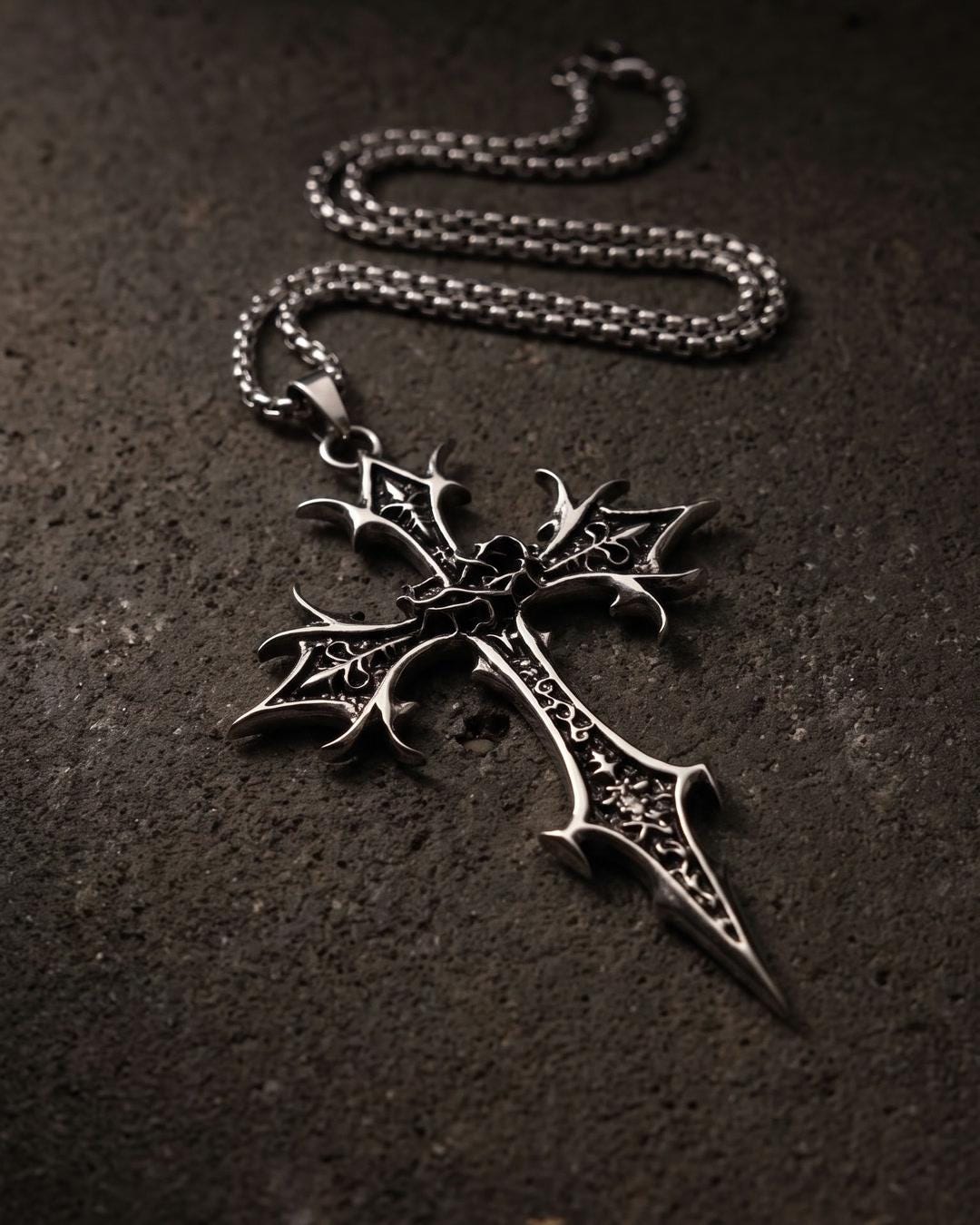 Close-up of gothic cross necklace showing barbed wings, dagger point, and blackened filigree on silver-tone finish