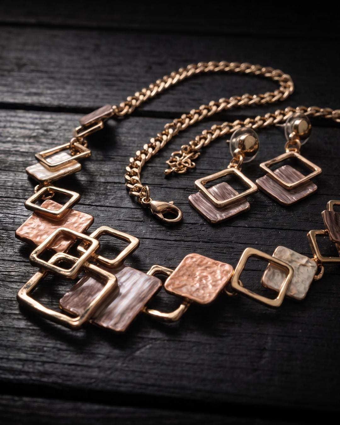 Flat lay of a geometric necklace and square drop earrings set in gold-tone with rose and mauve panels