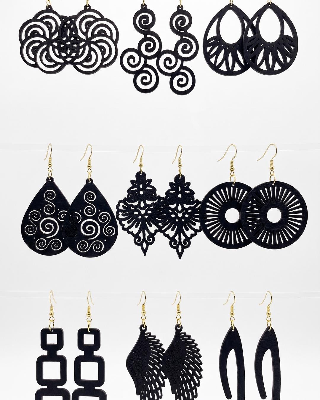 Flat lay of nine pairs of black drop earrings in matte wood with openwork cutouts arranged on a light surface