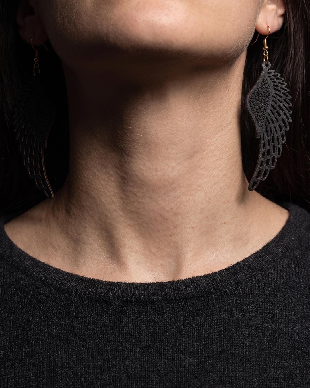 Black drop earrings with feathered wing cutouts worn on a model alongside a dark knit and velvet choker