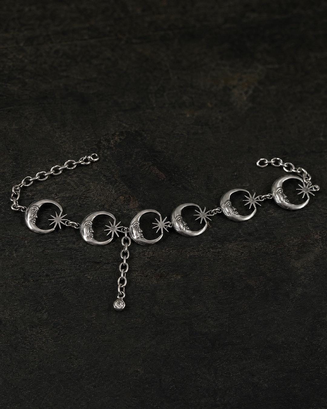 Crescent moon waist chain belt worn at the waist over a black slip skirt, rhinestone drop visible at center front.