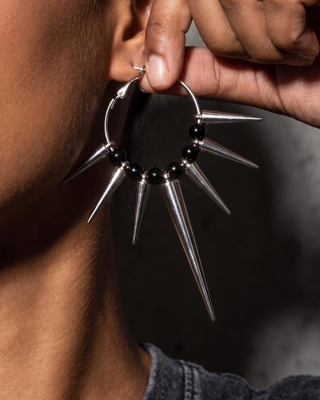 Close-up of silver spiked earrings showing seven graduated cone spikes and black beads on a hoop