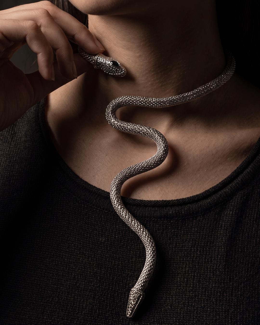 Silver serpent wrap collar worn high on the throat over bare skin with a deep neckline.