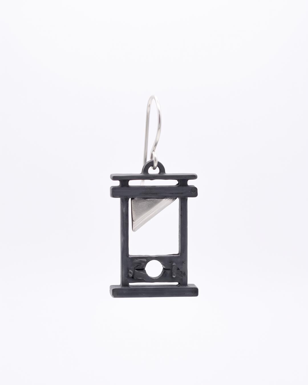 Close-up of vintage guillotine drop earrings showing oxidized grey frame and silver blade on white background