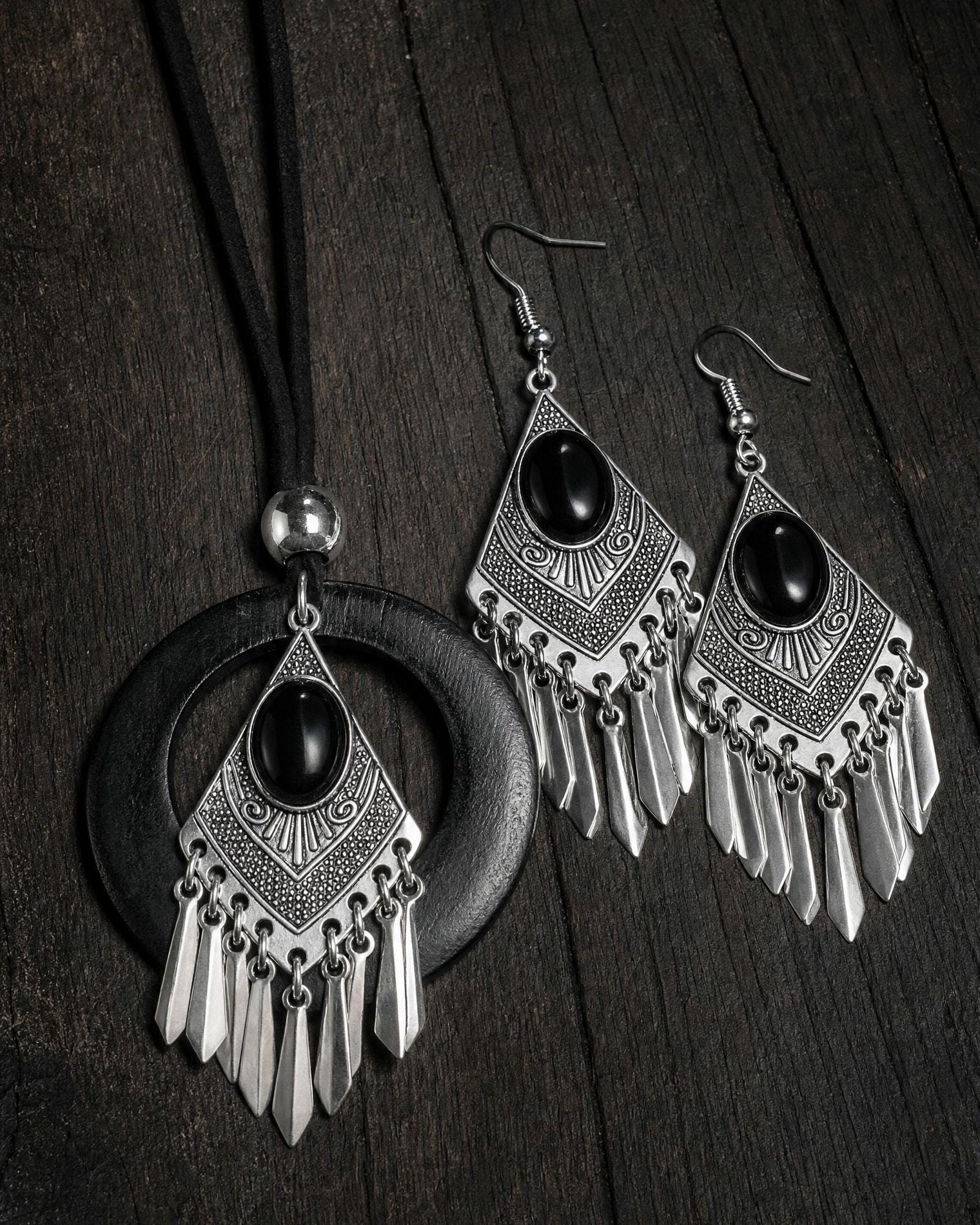 Dark feminine goth earrings with spike tassels hanging against a dark fabric background