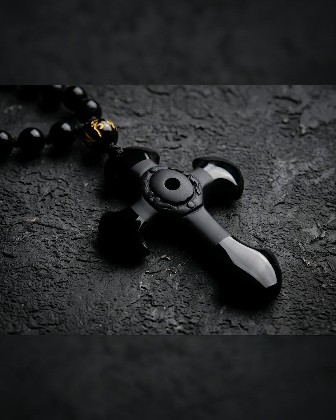 Close view of a black stone cross necklace with flared arms and a pierced center medallion on a black bead strand
