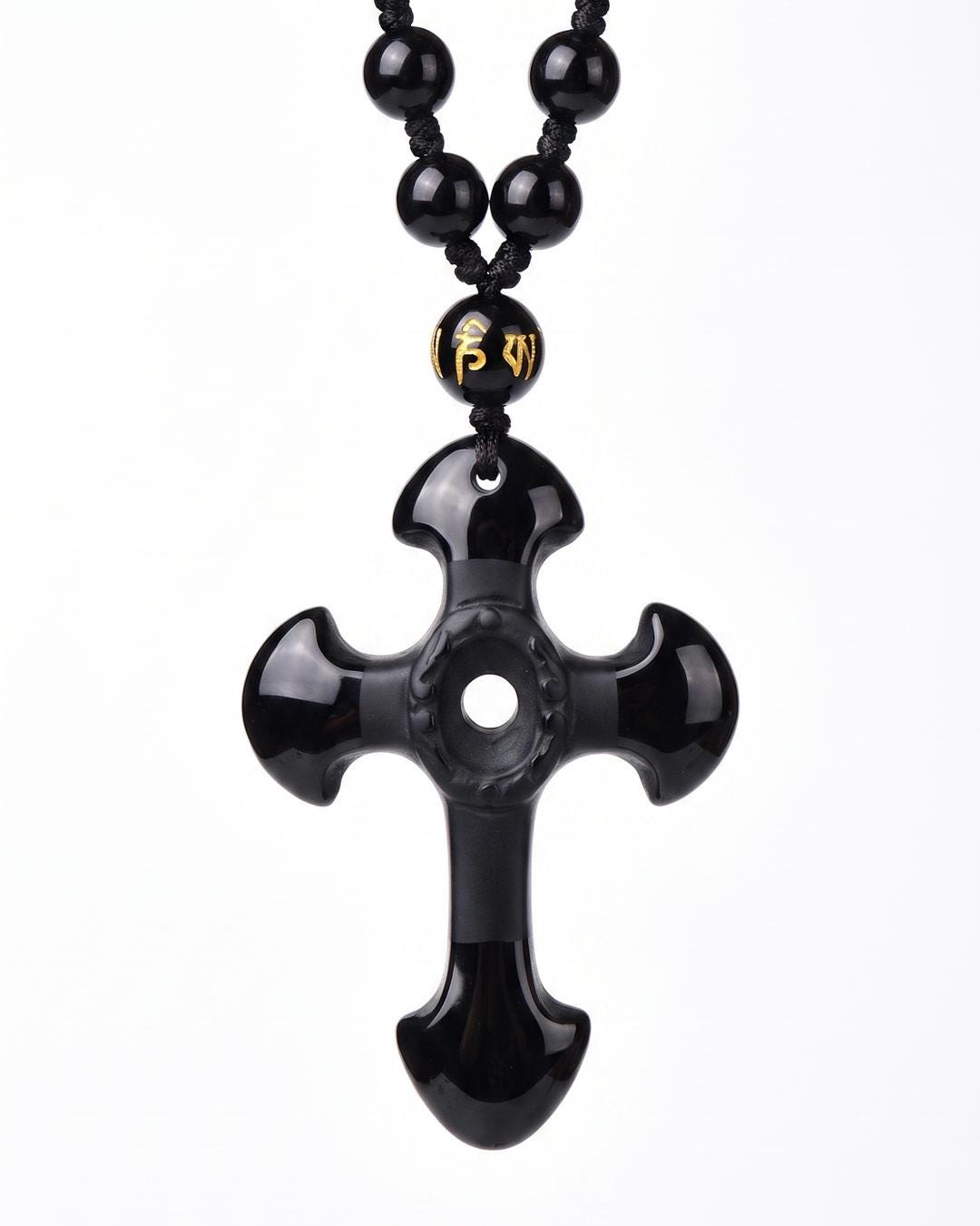 Black stone cross necklace worn over a black slip dress, pendant resting against bare skin