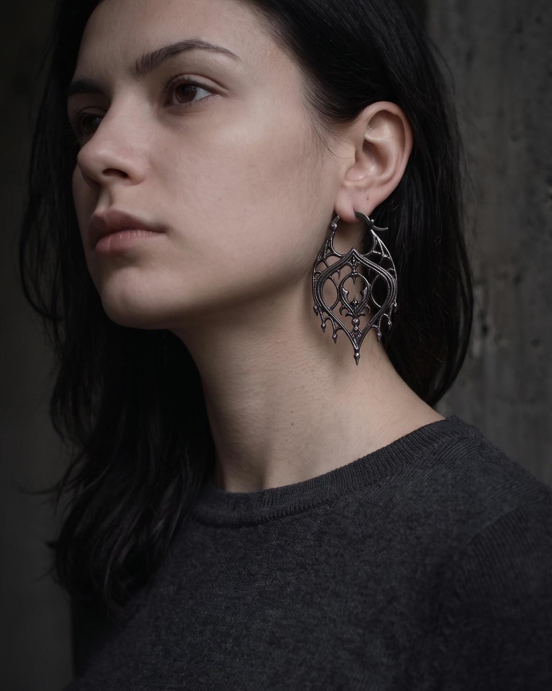 Black teardrop earrings worn against a model's neck, hair pulled back to show the tracery panel
