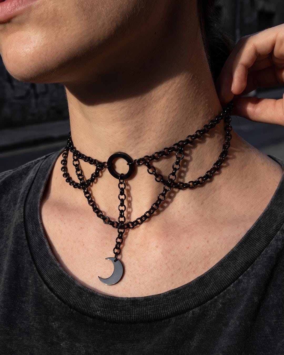 Close-up of a black layered moon pendant choker with doubled rolo chains and a crescent charm against a plain background