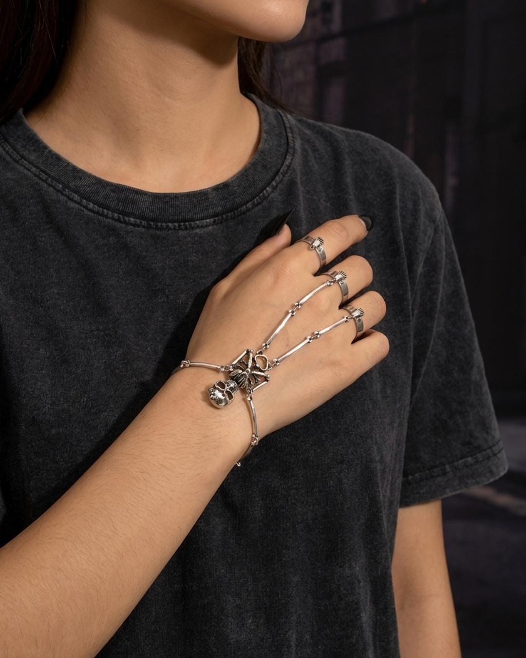 Antiqued silver skeleton hand chain worn on the back of a hand against bare skin with dark nails