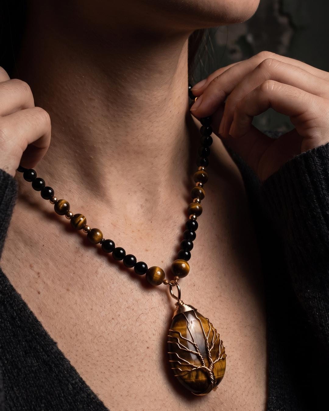 Close-up of a tiger's eye tree of life beaded necklace showing gold-tone wire wrap over a brown teardrop stone