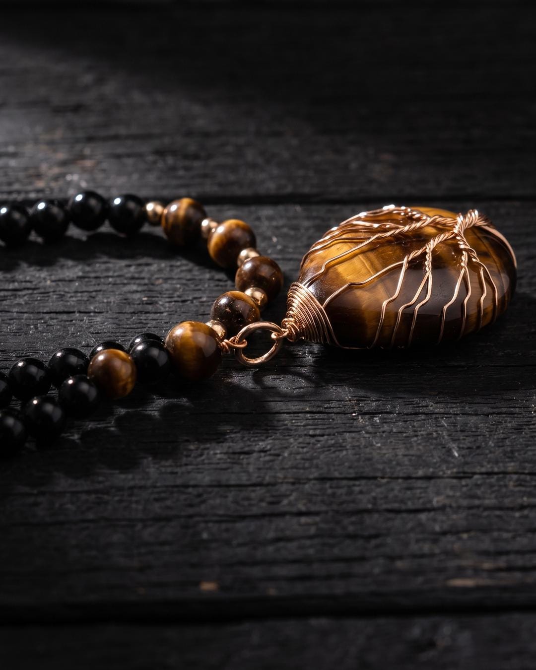 Tiger's eye tree of life beaded necklace laid flat on a dark surface with black beads visible