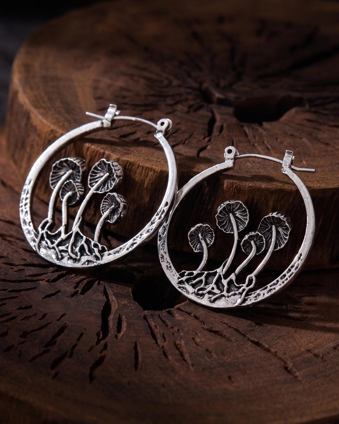 Close-up of antiqued silver mushroom hoop earrings showing three ribbed mushroom caps on curved stems inside an openwork hoop