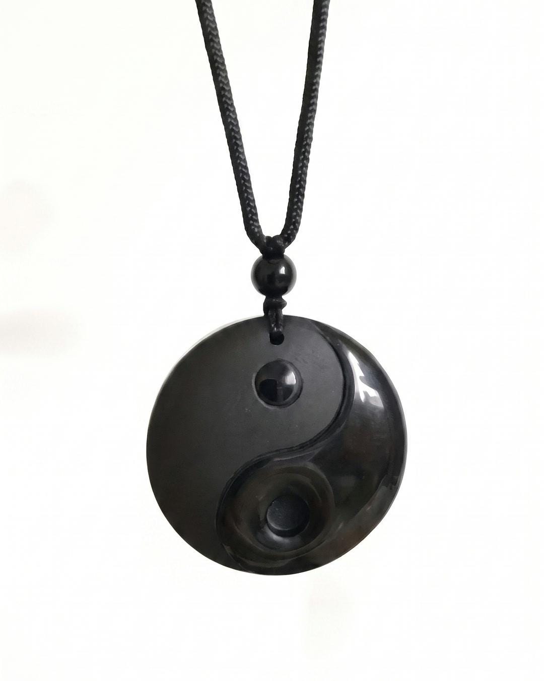 Black stone yin yang pendant necklace hanging against a dark fabric background on braided cord