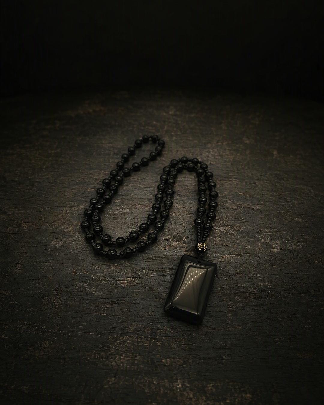 Close-up of a black slab pendant beaded necklace showing the polished rectangular pendant and gold-lettered accent bead