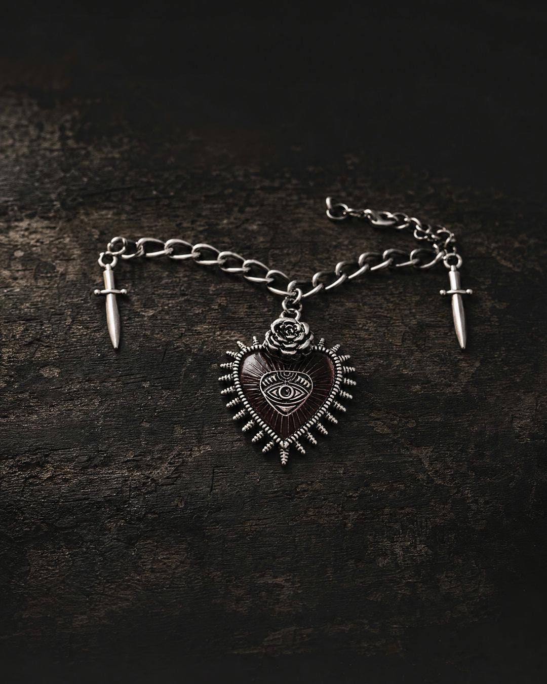Sacred heart dagger choker necklace flat lay, red enamel heart, rose crown, twin daggers, silver-tone curb chain.